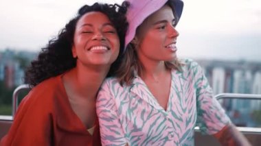 Two smiling multinational young women talking and riding a ferris wheel in adventure park