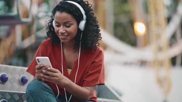 Laughing Hispanic Curly Haired Woman Listening Music Headphones While Sitting — Stok Video