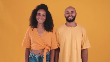 Smiling hispanic couple looking at the camera while standing in the yellow studio