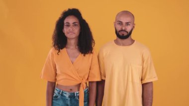 Displeased hispanic couple showing silence gesture at the camera in the yellow studio
