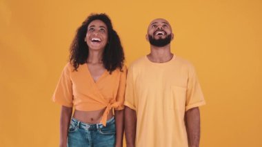 Cheerful hispanic couple looking up and at the camera in the yellow studio