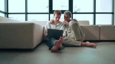 Lovely gay couple working on laptop and talking while sitting on the floor at home