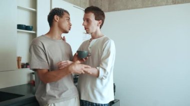 Handsome multinational gay couple talking and holding hands while standing in the kitchen