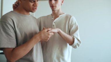 Lovely multinational gay couple talking and kissing hand while standing in the kitchen