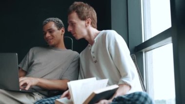 Smiling multinational gay couple looking at laptop while talking at home