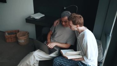 Laughing multinational gay couple looking at laptop while talking at home