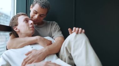 Positive multinational gay couple reading book and talking at home