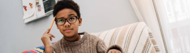 Black puzzled boy doing homework while sitting on sofa at home