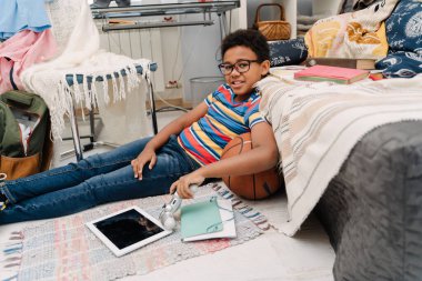Black boy in eyeglasses laughing while sitting on floor at home