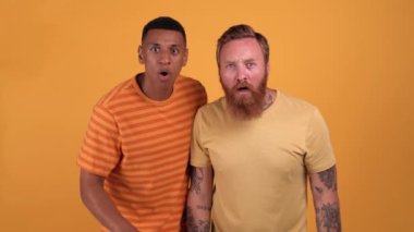 Pretty multinational men looking at the camera and getting upset in the yellow studio