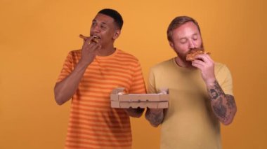Pretty multinational men eating pizza while standing in the yellow studio