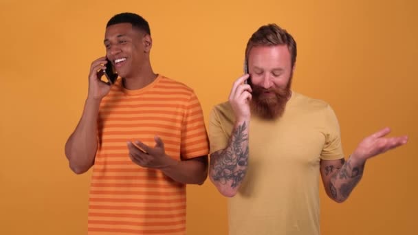 Happy Multinational Men Talking Phones While Standing Yellow Studio — Vídeo de stock