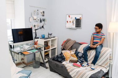 Black boy in eyeglasses sitting with tablet computer on sofa at home