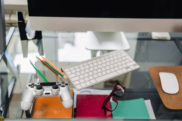 Photo of computer and joystick on glass desk indoors