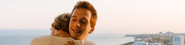 European gay couple smiling and hugging on balcony at home