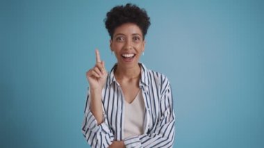 Smiling hispanic curly haired woman having an idea while standing in the blue studio
