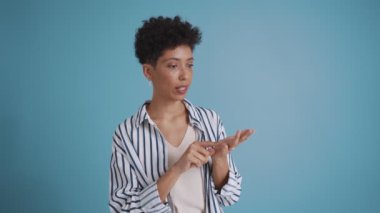 Smiling hispanic curly haired woman counting on fingers and looking at the camera in the blue studio