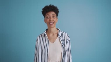 Positive hispanic curly haired woman laughing at the camera in the blue studio