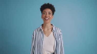 Happy hispanic curly haired woman talking and rejoicing at the camera in the blue studio