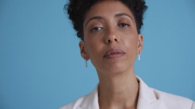 Face of pensive hispanic curly haired woman agrees with something at the camera in the blue studio