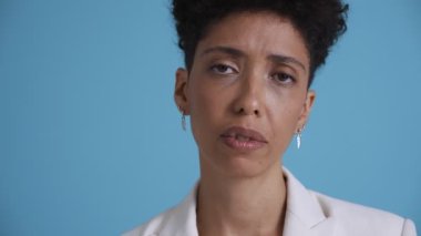 Face of sad hispanic curly haired woman looking at the camera in the blue studio
