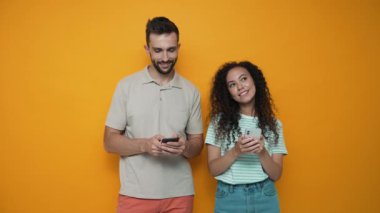 Funny brunette couple typing on phones while standing in the yellow studio