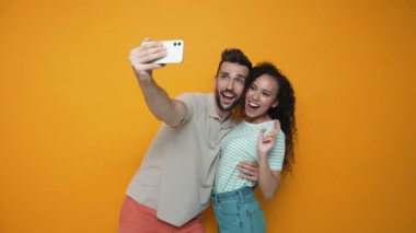 Cheerful brunette couple making selfie on phone while standing in the yellow studio