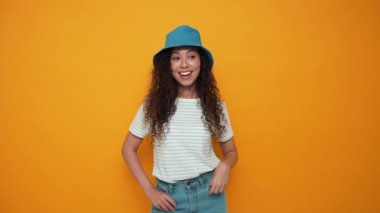 Surprised brunette curly haired woman wearing panama hat pointing at the copyspace in the yellow studio