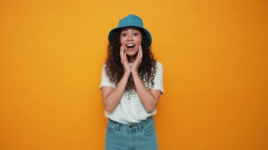 Cute brunette curly haired woman wearing panama hat looking at the camera in the yellow studio