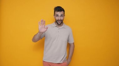 Smiling brunet man wearing t-shirt greeting at the camera in the yellow studio