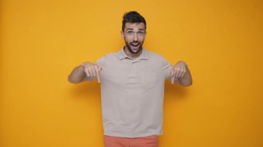 Laughing brunet man wearing t-shirt pointing fingers down and looking at the camera in the yellow studio