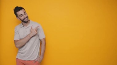 Smiling brunet man wearing t-shirt pointing fingers to the copyspace and looking at the camera in the yellow studio