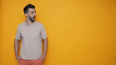 Shocked brunet man wearing t-shirt looking at the copyspace in the yellow studio