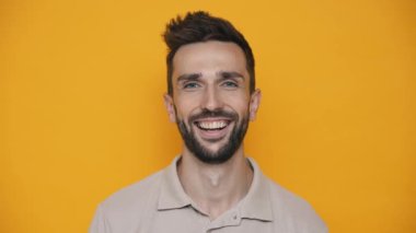 Laughing brunet man wearing t-shirt looking at the camera while standing in the yellow studio