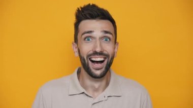 Surprised brunet man wearing t-shirt looking at the camera in the yellow studio