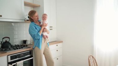 Pretty blonde mother talking with a small child in her arms in the kitchen