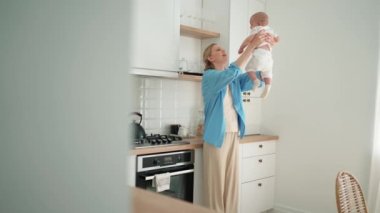 Happy blonde mother playing with a small child in her arms in the kitchen
