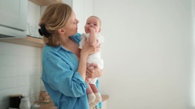Positive blonde mother talking with a small child in her arms in the kitchen
