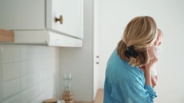 Smiling blonde mother talking and hugging her small child in her arms in the kitchen