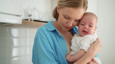 Lovely blonde mother wipes her child's face in the kitchen
