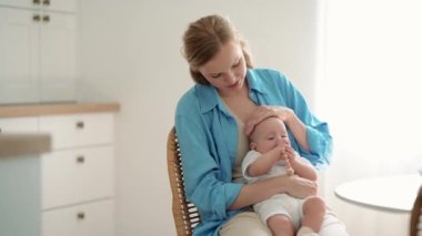 Pleased blonde mother with a small child in her arms sitting in the kitchen