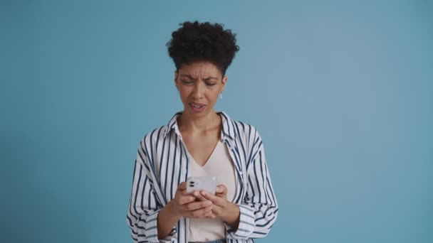 Displeased Hispanic Curly Haired Woman Texting Phone While Standing Blue — Stock videók