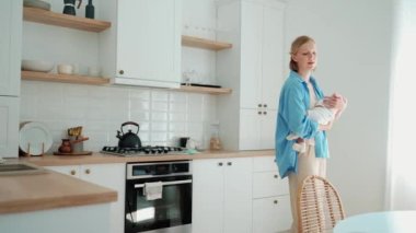 Lovely blonde mother rocking a baby in her arms in the kitchen