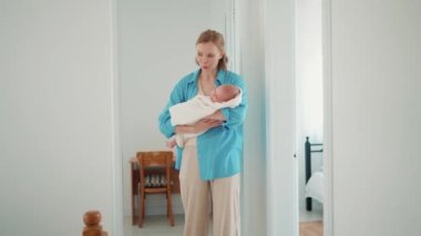 Smiling blonde mother rocking a baby in her arms at home