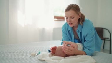 Lovely blonde mother talking with her little baby lying on the bed at home