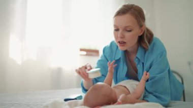 Lovely blonde mother talking and brushing hair her little baby lying on the bed at home