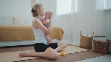 Lovely blonde mother playing with her small child after yoga exercise at home