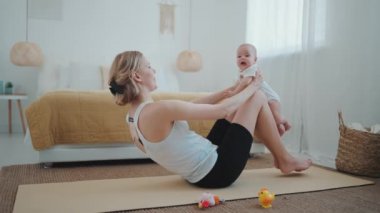 Laughing blonde mother playing with her small child after yoga exercise at home