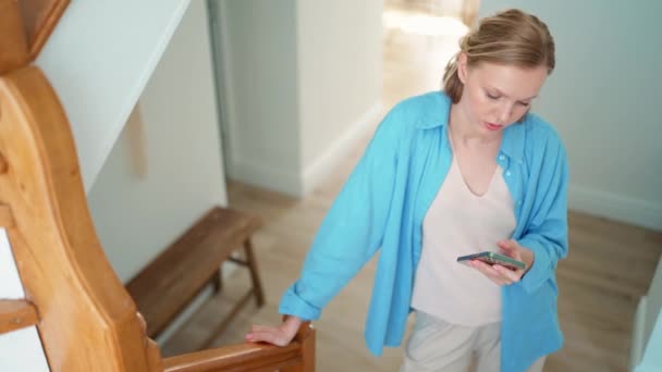 Positive Blonde Woman Typing Phone While Standing Indoors Home — Stockvideo