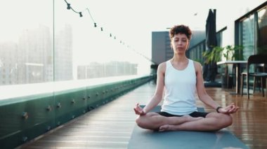 Confident African sporty woman doing meditation with closed eyes on the yoga mat outdoors